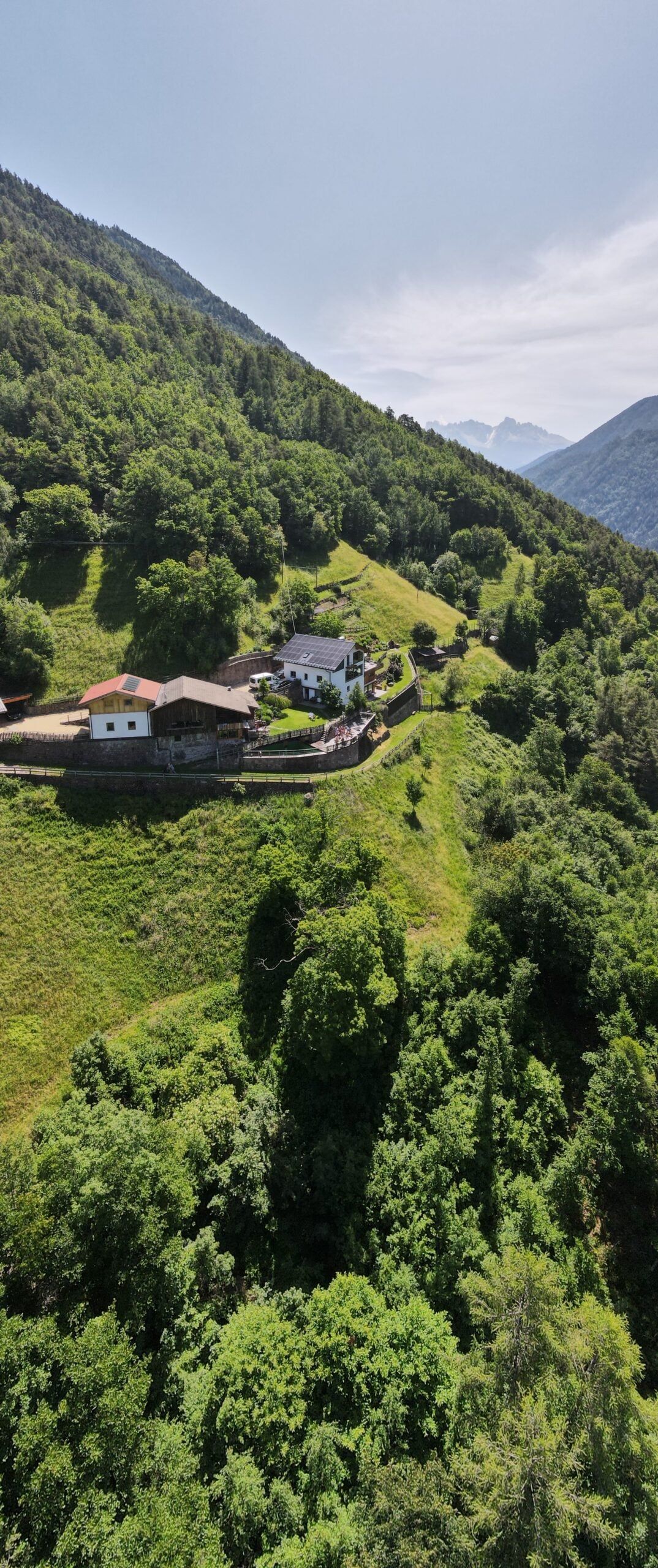 Luftaufnahme der Hofgebäude des Brentwaldhofs auf einer Wiesenterrasse am steilen Hang